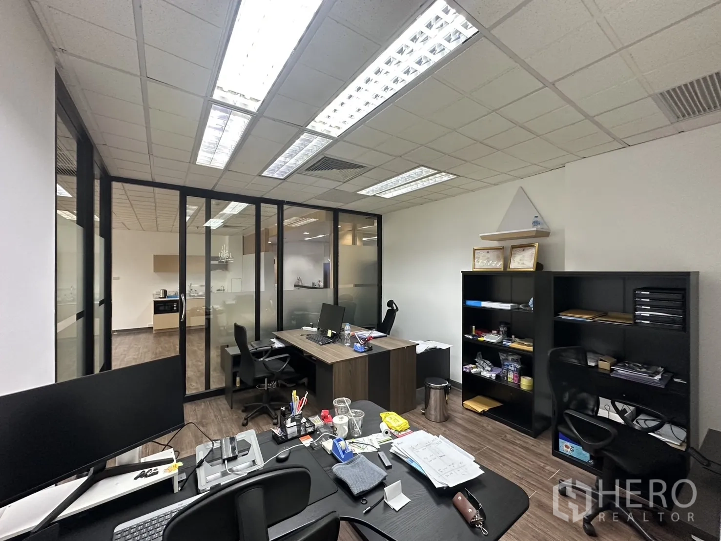Office Space for rent - Private management office with glass walls, desks, and shelving units.
