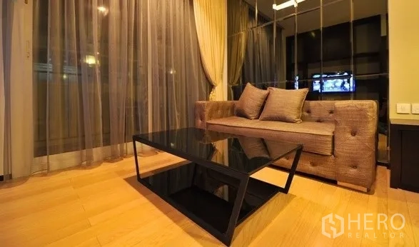 คอนโด ให้เช่าในKhlong Toei, Bangkok - ห้องนั่งเล่นพร้อมโซฟาบุผ้า โต๊ะกลางกระจกสีดำ และผ้าม่านโปร่งถึงพื้น