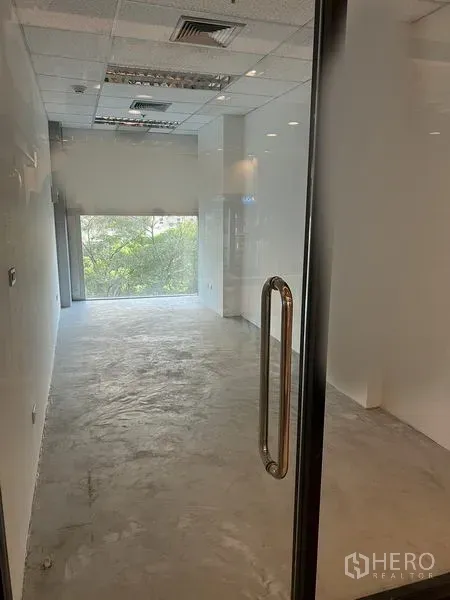 零售空间 出租在Bang Rak, Bangkok - 色隆邦拉区紧凑商铺，设玻璃门、抛光水泥地、白色墙面、吊顶与嵌灯，尽端大窗可见绿意景观。