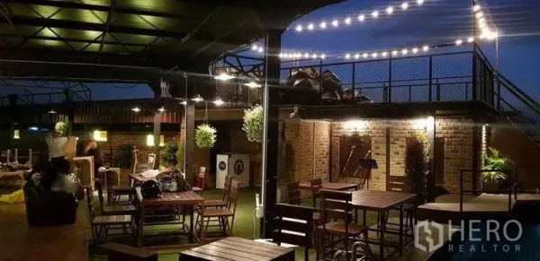 零售空间 出租在Khlong Toei, Bangkok - 屋顶用餐区，串灯、木质餐桌与砖墙，临近泳池。