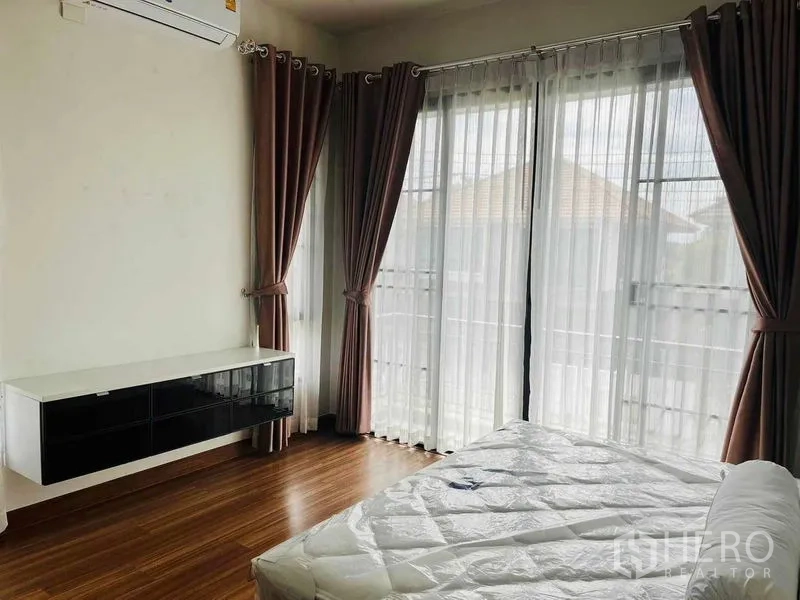 Detached House for rent or sale in Thanyaburi, Pathum Thani - Sunlit bedroom with floor-to-ceiling windows, sheer curtains and warm wood flooring.