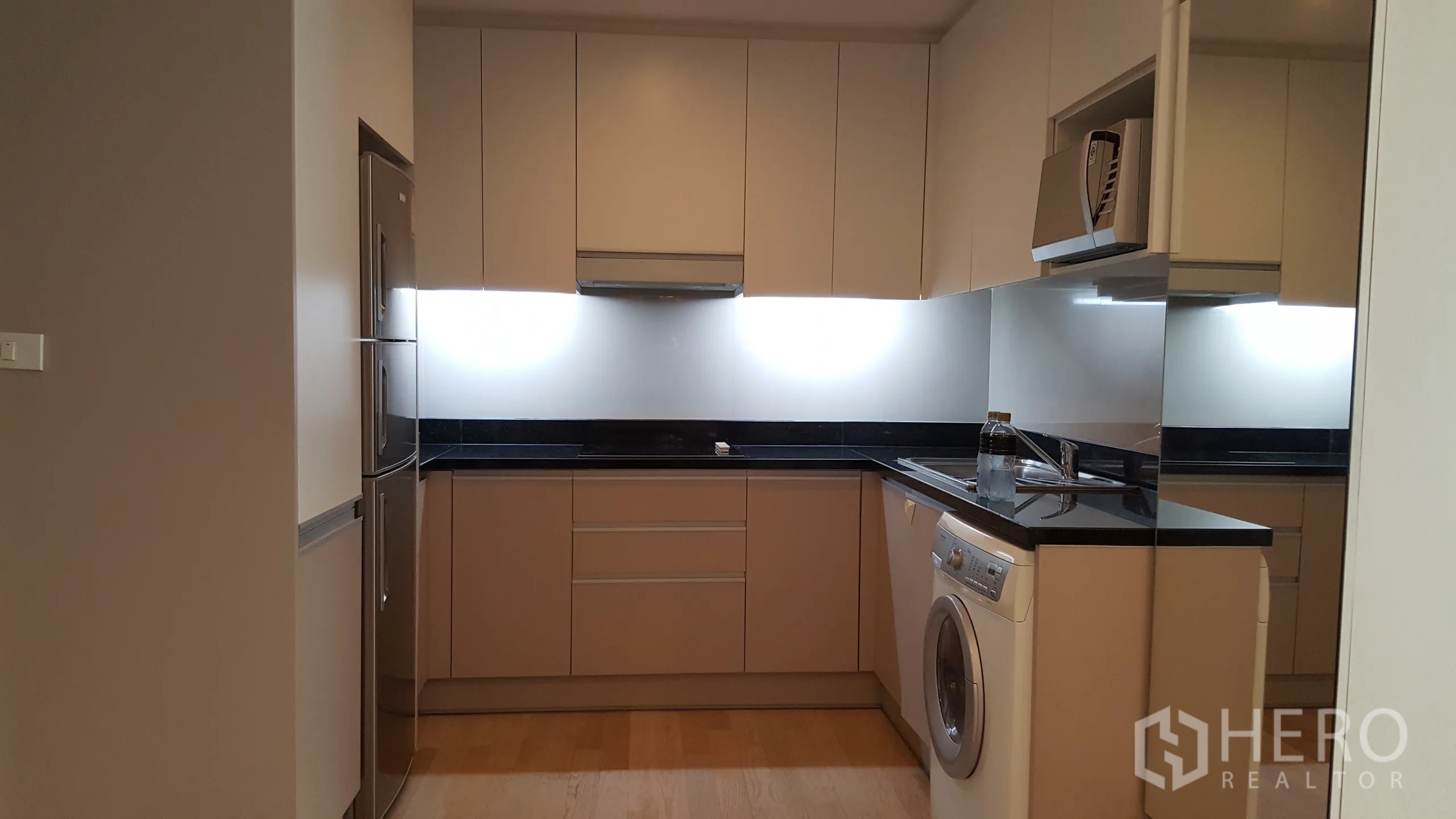 Condominium for rent in Khlong Toei, Bangkok - Modern U-shaped kitchen with built-in cabinets, stone countertops, fridge and washing machine.