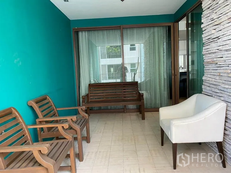 公寓 出租在Khlong Toei, Bangkok - 覆盖式阳台/日光房，青绿色墙面、石材装饰、木长椅与白色扶手椅。