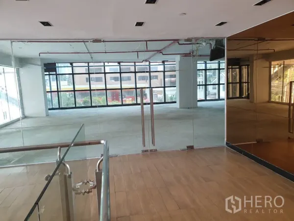 零售空间 出租在Watthana, Bangkok - 玻璃双开门入口，镜面墙与木地板，通向采光充足的零售区。