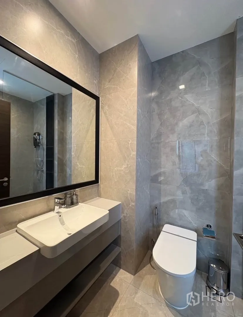 Detached House for rent in Suan Luang, Bangkok - Contemporary bathroom with large mirror, sleek vanity and toilet in gray finishes.