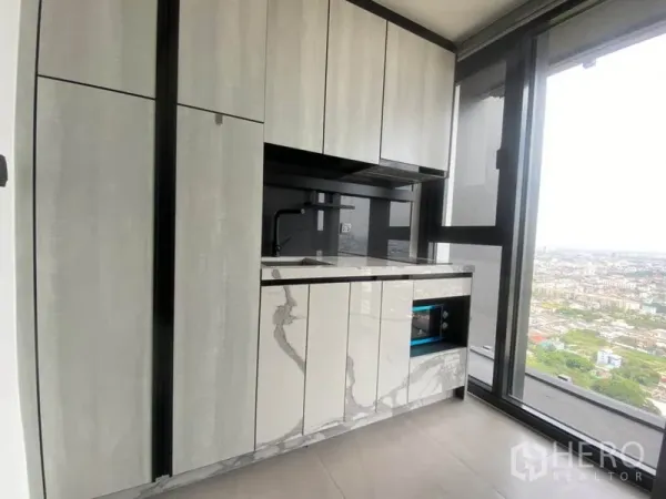 Condominium for rent in Phra Khanong, Bangkok - Compact modern kitchen with marble-look cabinetry beside a large window overlooking the Bangkok skyline.