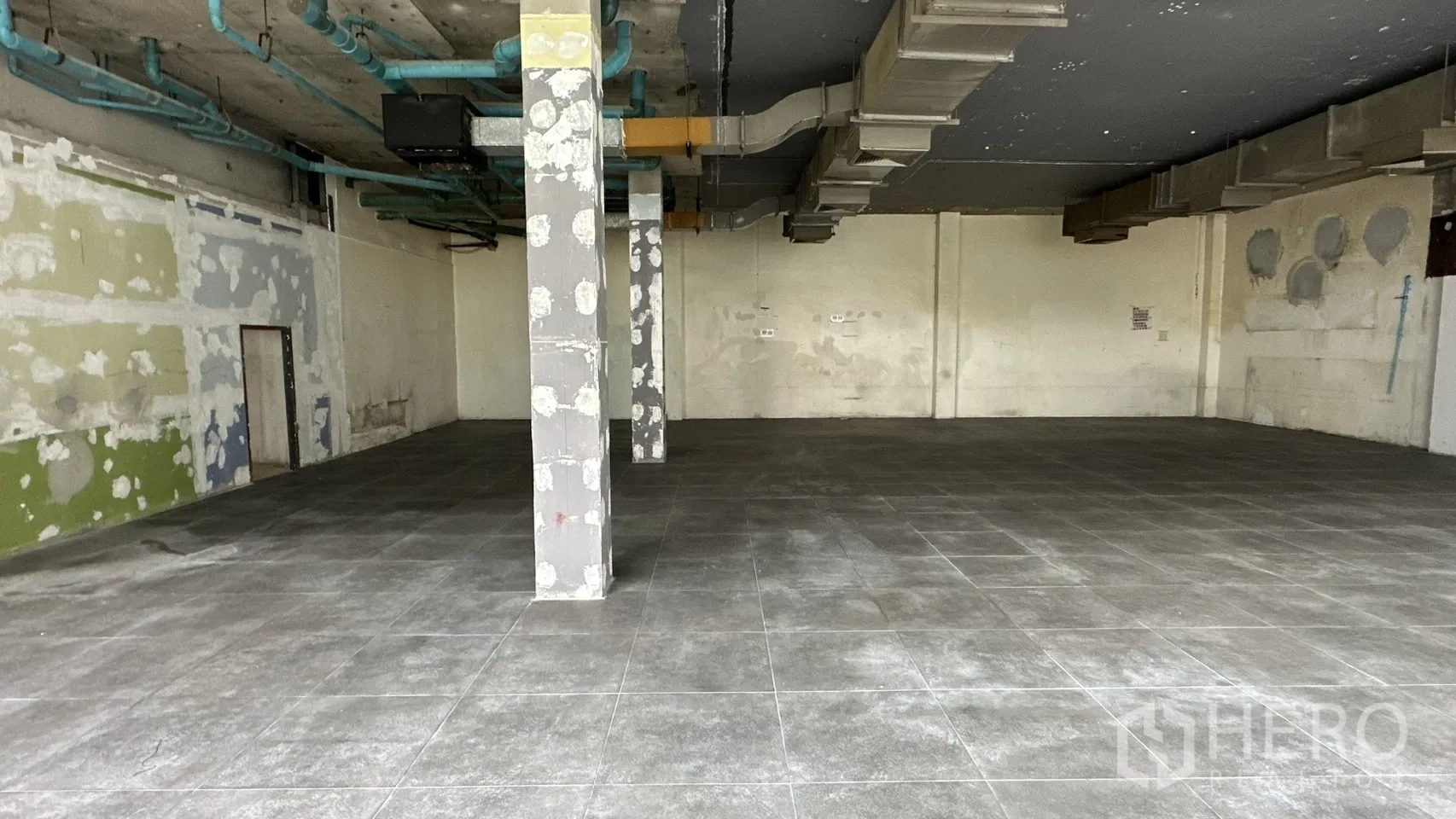 Retail Space for rent in Watthana, Bangkok - Central pillars with patched walls and blue service pipes along the ceiling.
