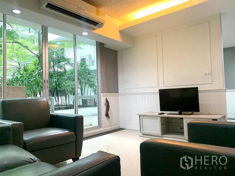 คอนโด ให้เช่าในKhlong Toei, Bangkok - ห้องนั่งเล่นมีชั้นวางทีวี โซฟาหนัง และประตูบานเลื่อนออกสู่ระเบียงวิวสวน