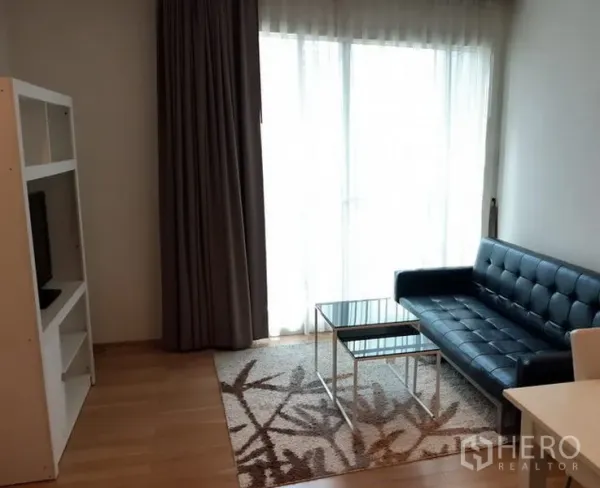 คอนโด ให้เช่าในKhlong Toei, Bangkok - ห้องนั่งเล่นสว่าง โซฟาหนังสีดำ โต๊ะกระจก ชั้นวางทีวี และหน้าต่างสูงจรดเพดานพร้อมผ้าม่าน