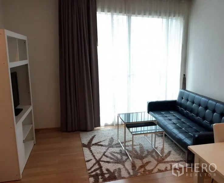 คอนโด ให้เช่าในKhlong Toei, Bangkok - ห้องนั่งเล่นสว่าง โซฟาหนังสีดำ โต๊ะกระจก ชั้นวางทีวี และหน้าต่างสูงจรดเพดานพร้อมผ้าม่าน