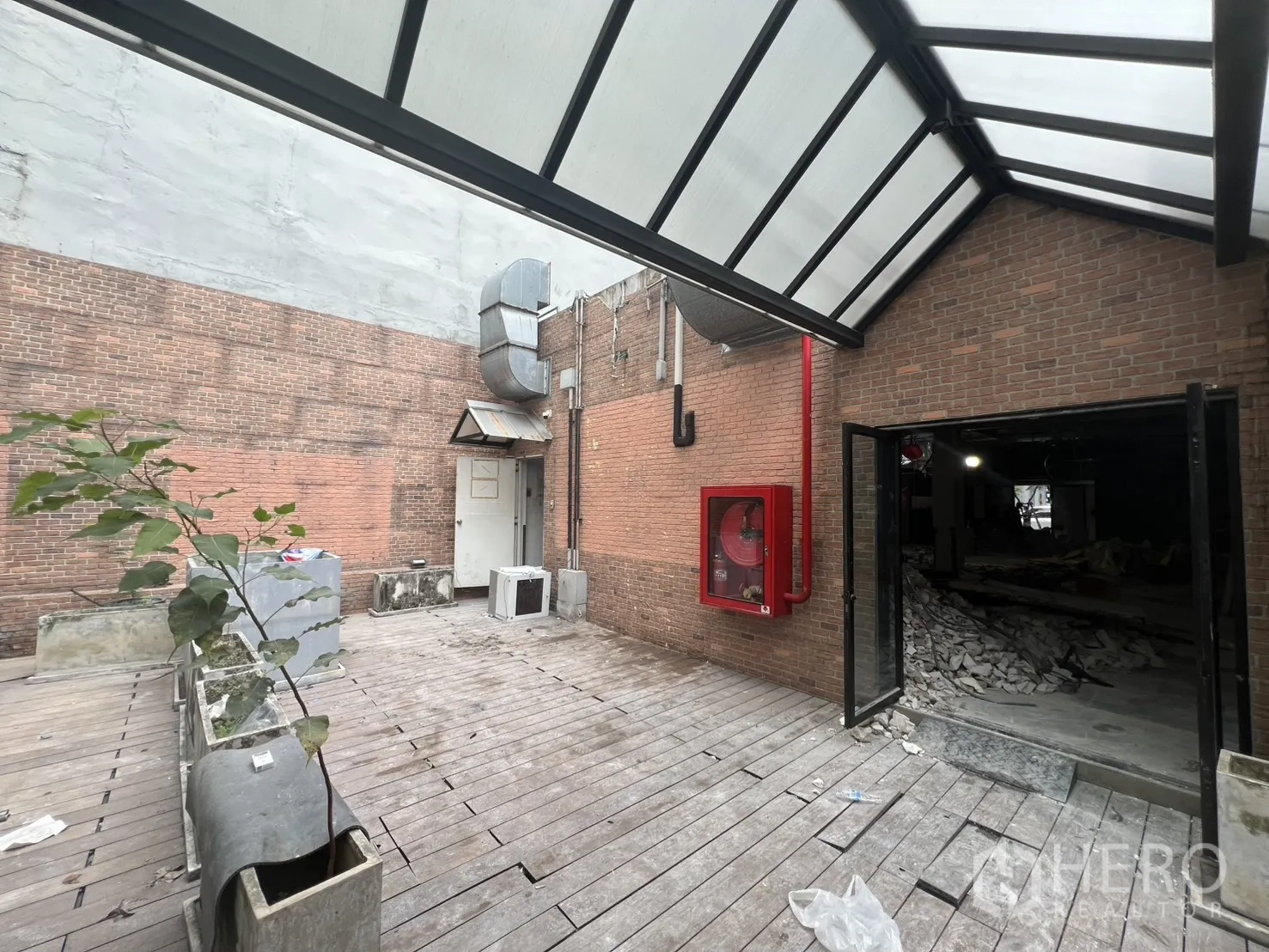 อาคารพาณิชย์ ให้เช่าในBang Rak, Bangkok - ลานระเบียงไม้ด้านหลังกำแพงอิฐ หลังคาโปร่งแสง และตู้สายฉีดดับเพลิงสีแดง