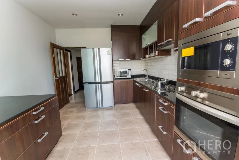 Condominium for rent in Sathon, Bangkok - Closed kitchen with dark wood cabinetry, built-in oven and stainless refrigerator.