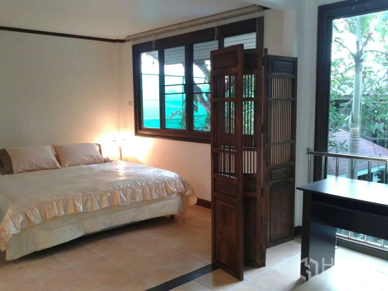 Detached House for rent in Suan Luang, Bangkok - Corner bedroom with large windows, a queen bed, and a wooden folding room divider.