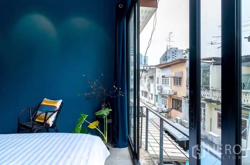 ทาวน์เฮาส์ for rent in Watthana, Bangkok - มุมห้องนอนผนังสีน้ำเงิน มีเก้าอี้และประตูกระจกบานเลื่อนออกสู่ระเบียงเห็นวิวชุมชน