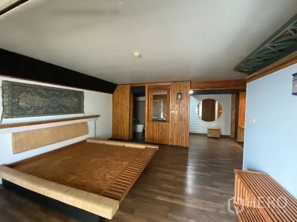 Condominium for rent or sale in Suan Luang, Bangkok - Primary bedroom with platform bed, wood-slat walls, ensuite access and dark wood flooring.