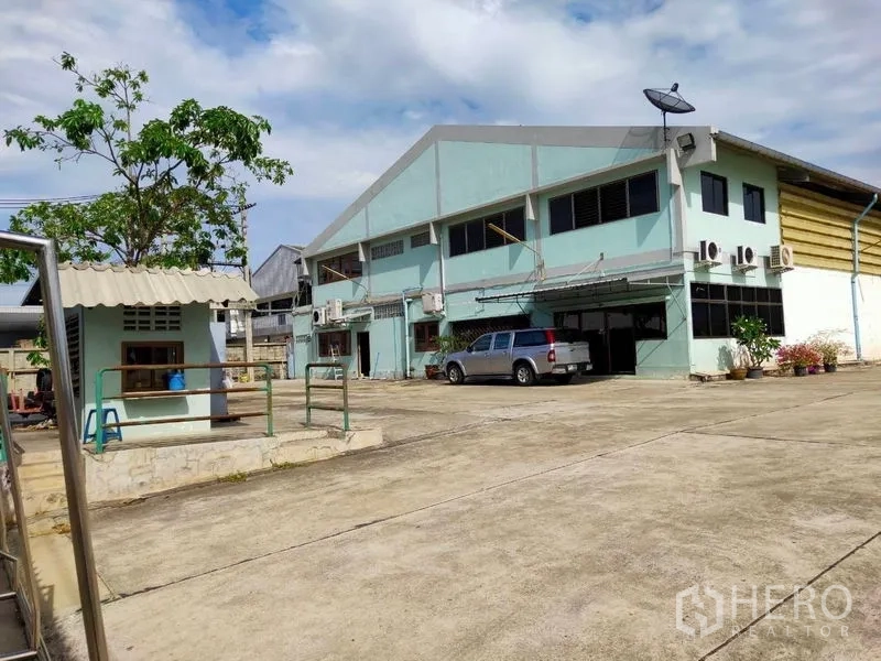คลังสินค้า ให้เช่าหรือขายในBang Bon, Bangkok - มุมหน้าคลังสินค้าสองชั้นสีเขียวฟ้า ลานคอนกว้าง มีรถกระบะ