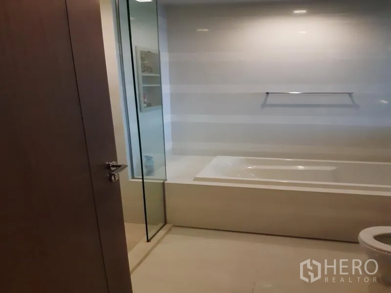 Condominium for rent or sale in Khlong Toei, Bangkok - Bright bathroom with built-in bathtub and clear glass divider.
