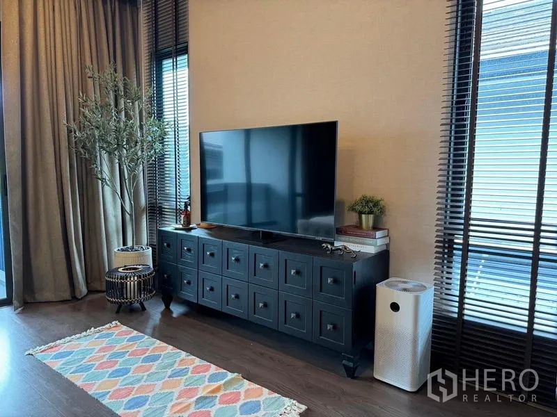 Detached House for rent in Bang Kapi, Bangkok - TV corner with large flat‑screen on a dark sideboard, tall blinds and decorative indoor plants.