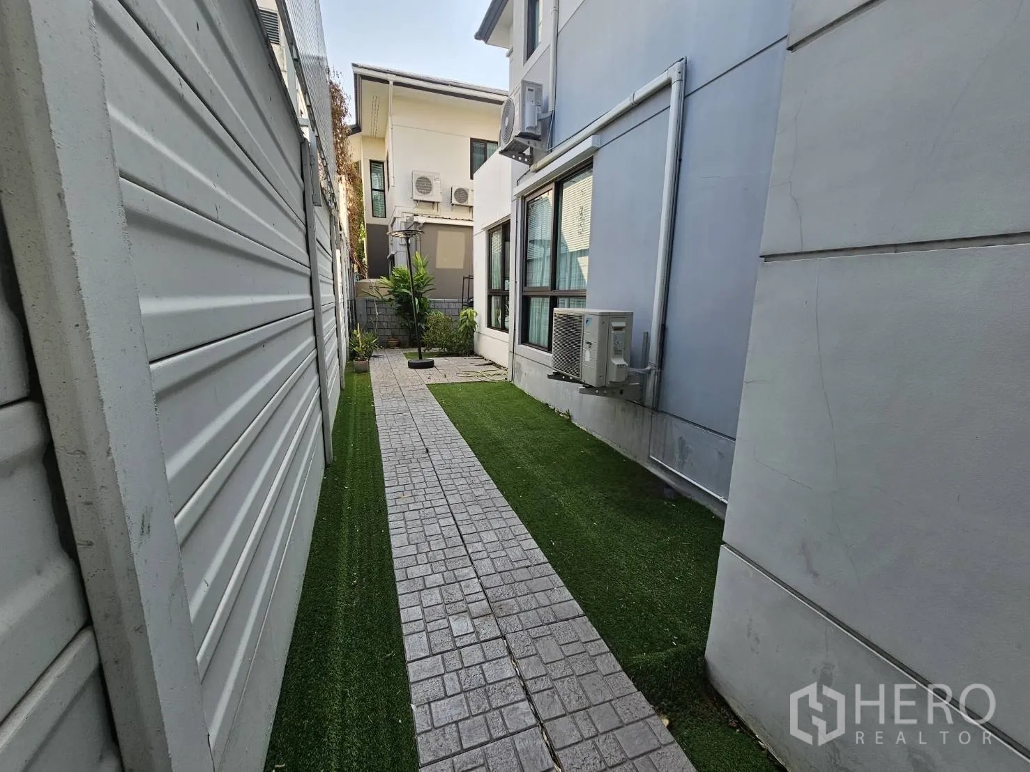 Detached House for rent in Wang Thonglang, Bangkok - Narrow side yard with paved path, artificial grass, and exterior air-conditioning units.