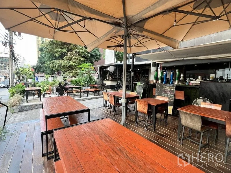 零售空间 出租在Watthana, Bangkok - 临街户外露台，木质餐桌、大片遮阳伞与绿植点缀。