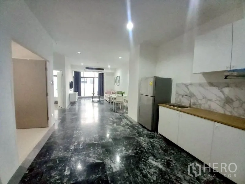 Condominium for rent in Watthana, Bangkok - Open kitchen with white cabinets, sink, refrigerator and marble splashback.