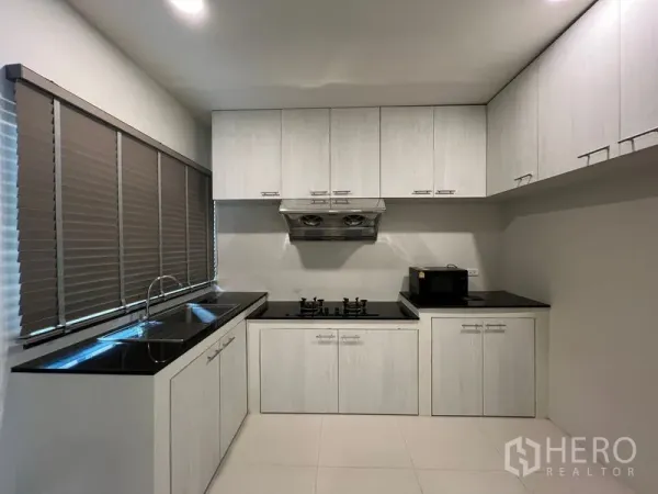 Detached House for rent in Bang Phli, Samut Prakan - L-shaped kitchen with white cabinetry, black countertops and gas hob.