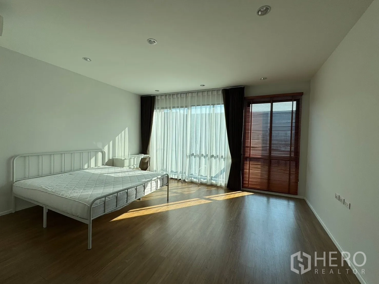 Townhouse for rent in Saphan Sung, Bangkok - Master bedroom with metal bed, floor-to-ceiling curtains and wood floor.