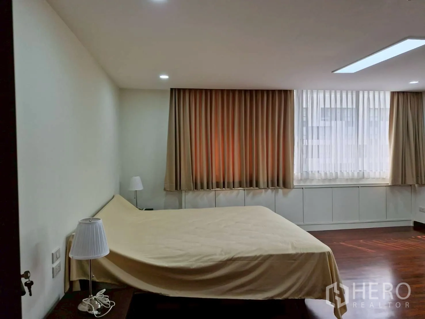 Condominium for rent in Khlong Toei, Bangkok - Bedroom with large bed, bedside lamps, thick curtains and wood floors.
