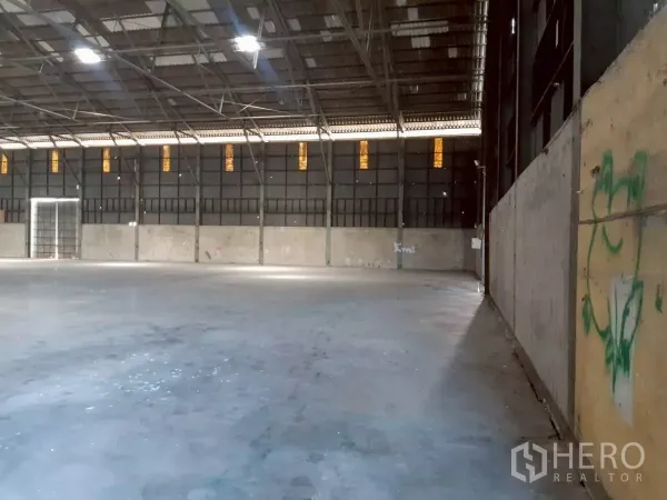 Warehouse for rent in Pak Kret, Nonthaburi - Corner view of warehouse wall with high ceiling, ventilation panels and heavy-duty concrete flooring.