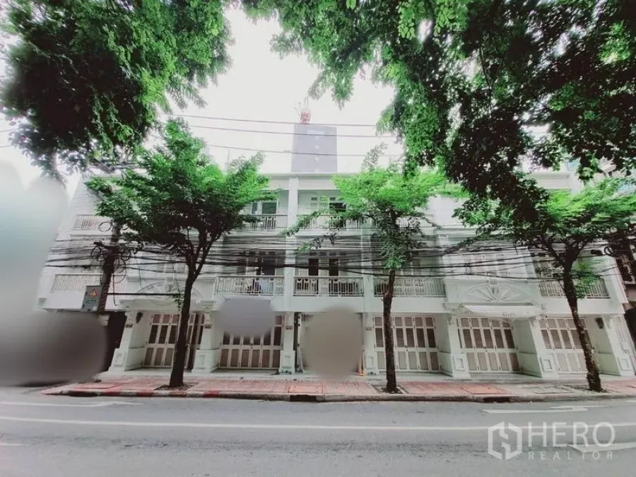 อาคารพาณิชย์ ให้เช่าในBang Rak, Bangkok - ด้านหน้าอาคารพาณิชย์หลายชั้นริมถนน มีระเบียงและประตูบานเฟี้ยมใต้ร่มไม้