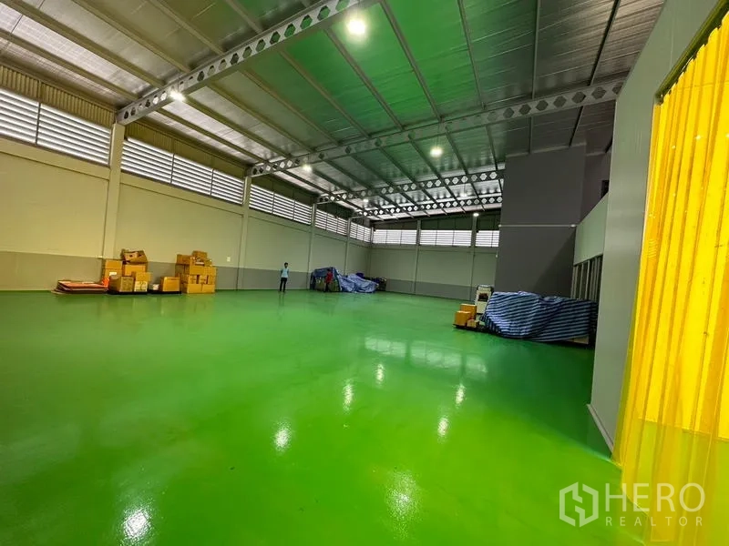โรงงาน ให้เช่าหรือขายในLam Luk Ka, Pathum Thani - โซนคลังสินค้าขนาดใหญ่ มีม่านพลาสติกเหลือง เพดานสูง และพื้นอีพ็อกซี่.