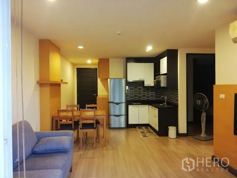 Condominium for rent in Watthana, Bangkok - Open-plan living area with dining set and black-and-white kitchenette with tiled backsplash.