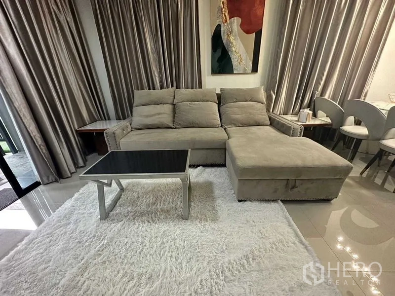 联排别墅 出租在Wang Thonglang, Bangkok - 客厅特写，灰色转角沙发、长绒地毯与茶几，落地窗帘。