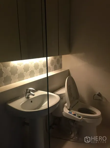 公寓 出租在Khlong Toei, Bangkok - 紧凑浴室，柱式洗手盆、镜柜与带喷洗功能马桶。