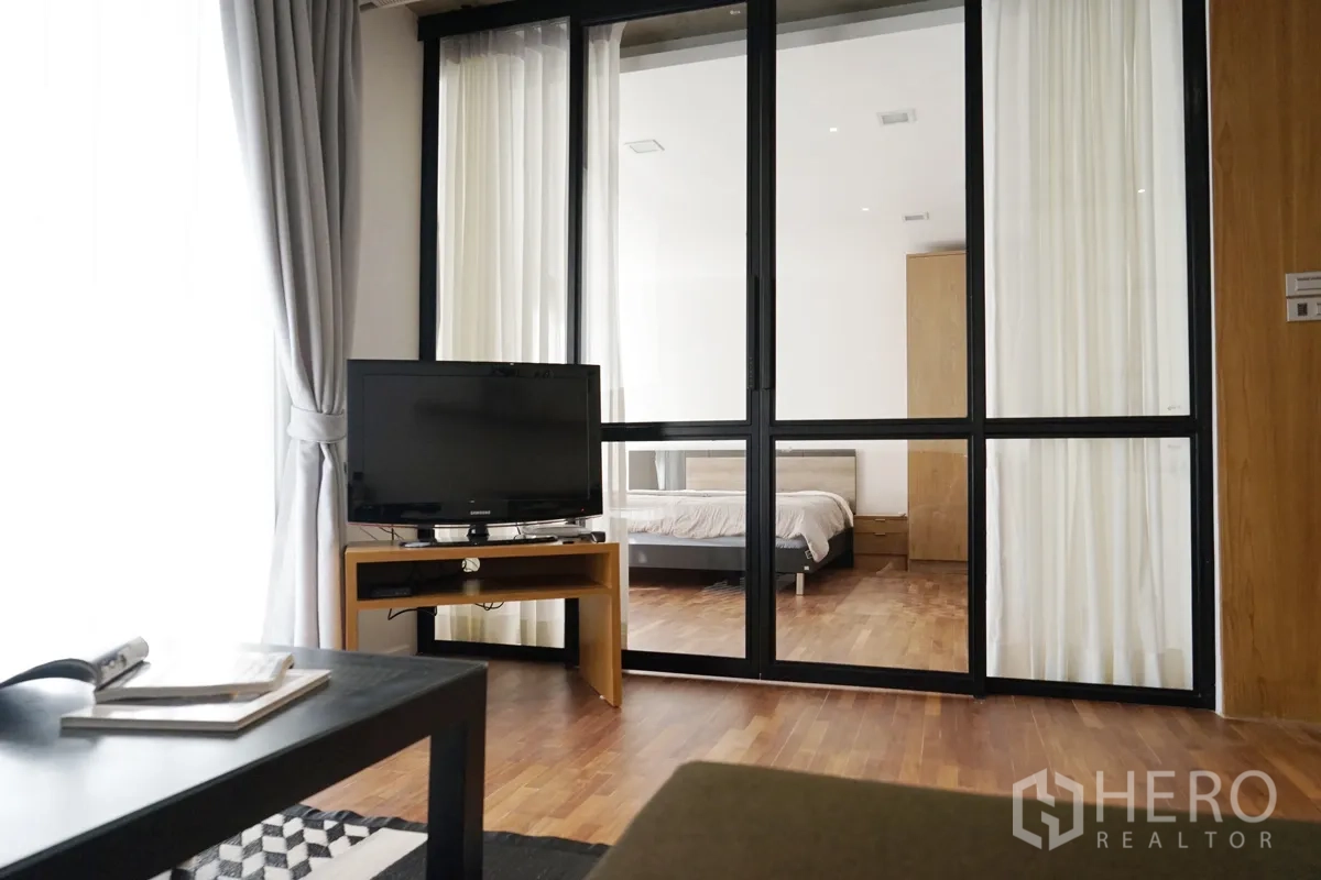คอนโด ให้เช่าในWatthana, Bangkok - ห้องนั่งเล่นมีทีวีและโต๊ะกลาง เชื่อมสู่ห้องนอนด้วยประตูกระจกกรอบสีดำแบบสไลด์