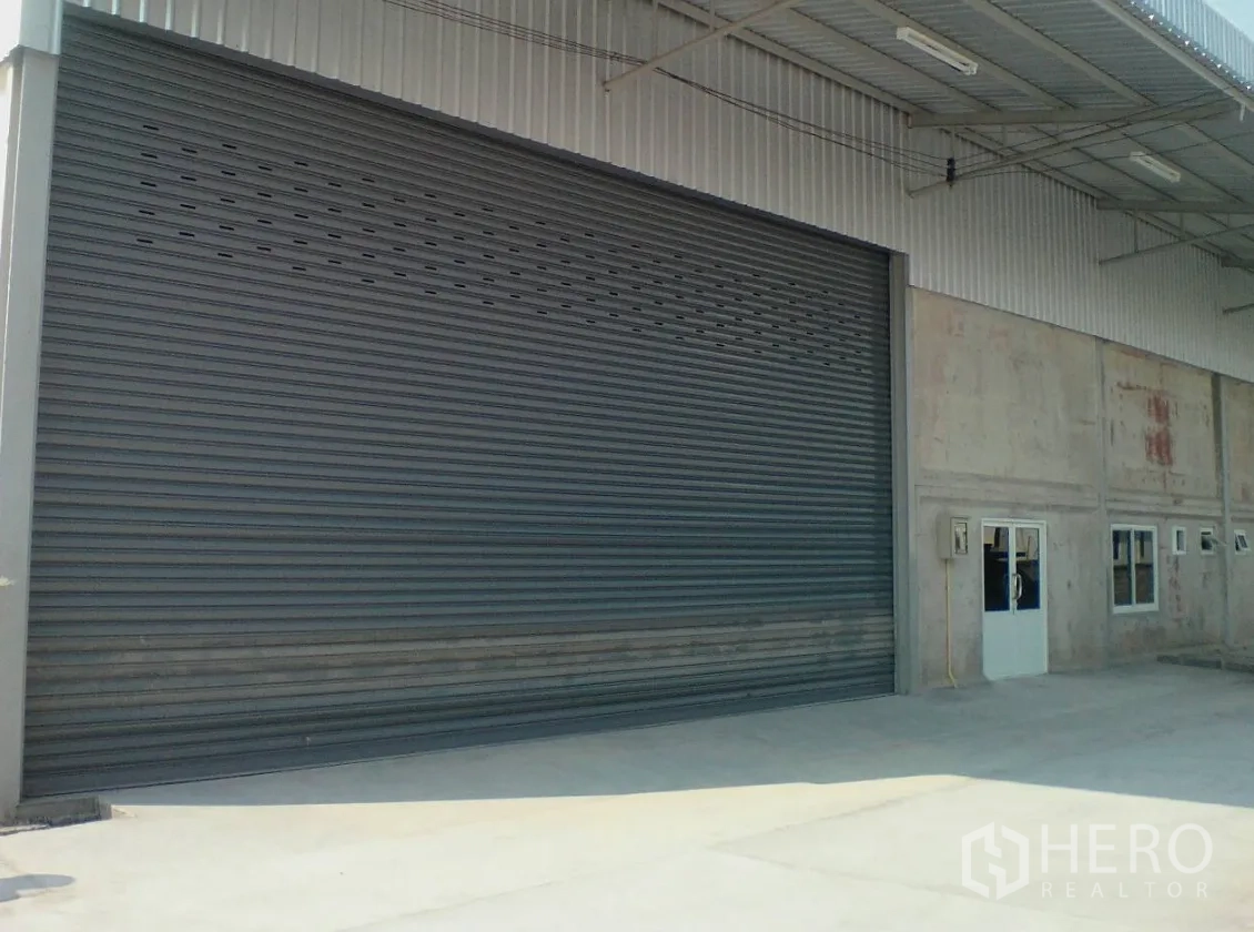 คลังสินค้า ให้เช่าในLam Luk Ka, Pathum Thani - ภาพใกล้ของประตูม้วนไฟฟ้าขนาดใหญ่ พร้อมประตูทางคนด้านข้าง