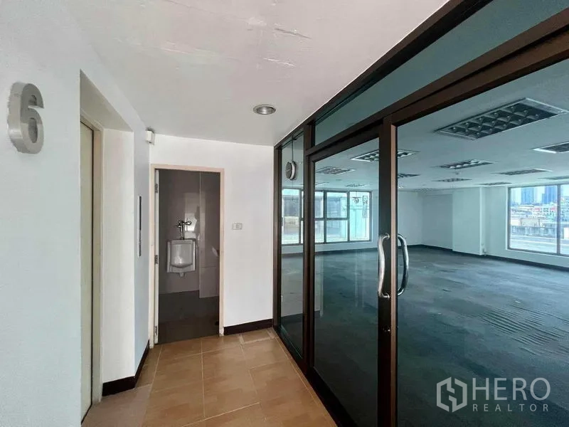 Shophouse for rent in Khlong San, Bangkok - Hallway with restroom and elevator leading to a glass-door office with city views.