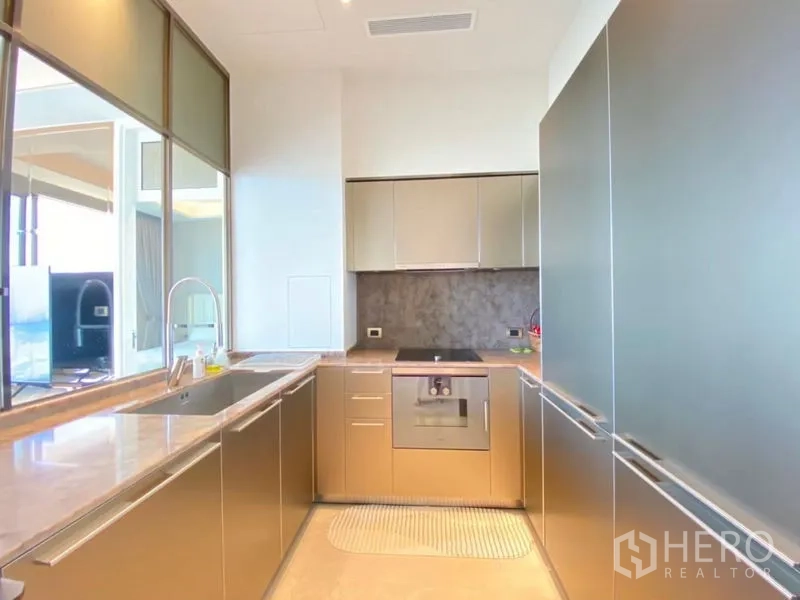 Condominium for rent in Khlong San, Bangkok - Modern U‑shaped kitchen with stone countertops, built‑in oven, and sleek cabinetry.