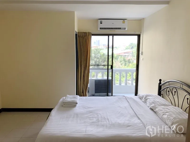 Apartment for rent in Suan Luang, Bangkok - Bedroom with large sliding doors to a balcony, air conditioning and leafy neighborhood views.