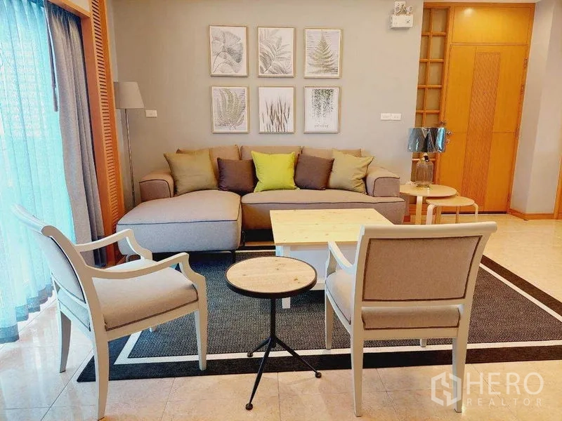 房间 出租 - 舒适客厅一角，L形沙发、两把扶手椅、叠桌与植物装饰画。