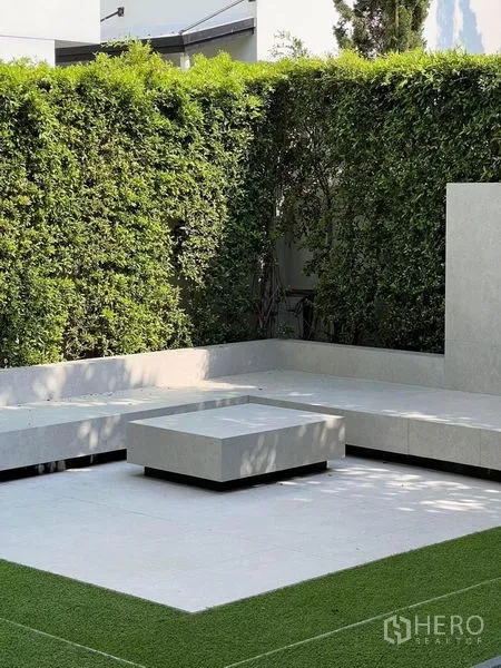 Detached House for sale in Samut Prakan - Outdoor terrace with built-in concrete bench and table bordered by green hedges.