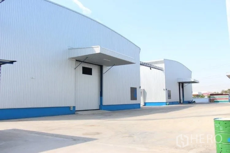 Warehouse for rent in Pathum Thani - Exterior of modern steel warehouses with curved roofs, loading canopies and a spacious paved yard.