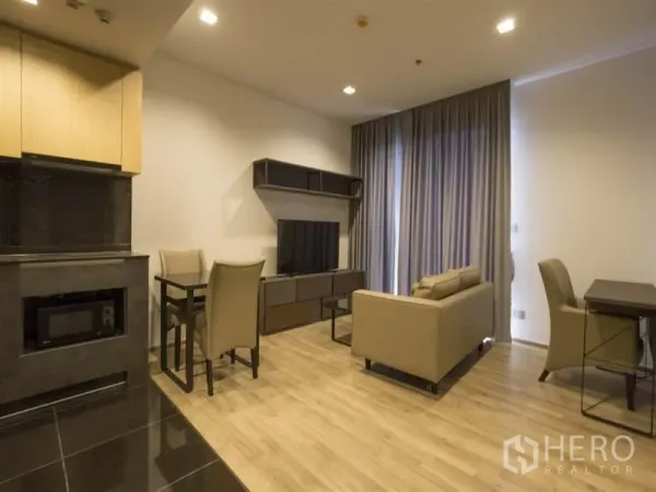 Condominium for rent in Chatuchak, Bangkok - Living and dining zone with TV wall unit, two-seat sofa, work desk, and kitchenette.