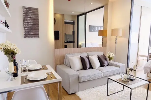 Condominium for sale in Watthana, Bangkok - Living space with sofa and dining table facing a glass partition to the bedroom.