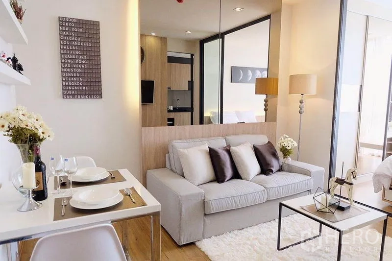 Condominium for sale in Watthana, Bangkok - Living space with sofa and dining table facing a glass partition to the bedroom.