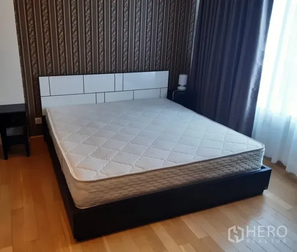 Condominium for rent in Khlong Toei, Bangkok - Bedroom with queen bed, feature wallpaper, wood flooring, and daylight from a large window.