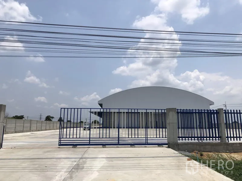 Factory for rent or sale in Lat Lum Kaeo, Pathum Thani - Blue steel entrance gate opening to a spacious forecourt and perimeter wall.