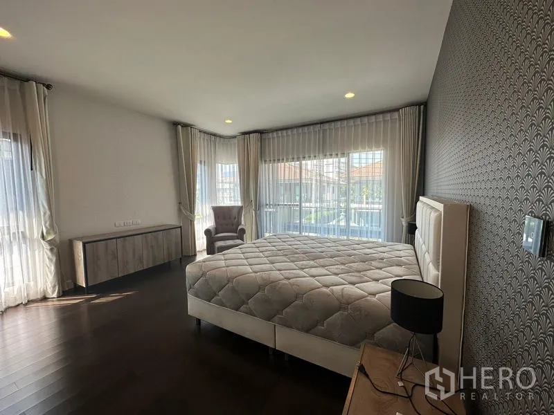 บ้าน ให้เช่าหรือขายในLam Luk Ka, Pathum Thani - ห้องนอนมุมกระจก พร้อมหน้าต่างบานใหญ่ ผ้าม่านโปร่ง ผนังลาย และเก้าอี้อาร์มแชร์