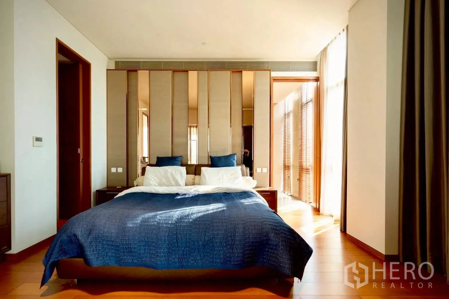 Condominium for sale in Sathon, Bangkok - Bedroom with blue bedding, mirrored headboard panels, and abundant natural light.