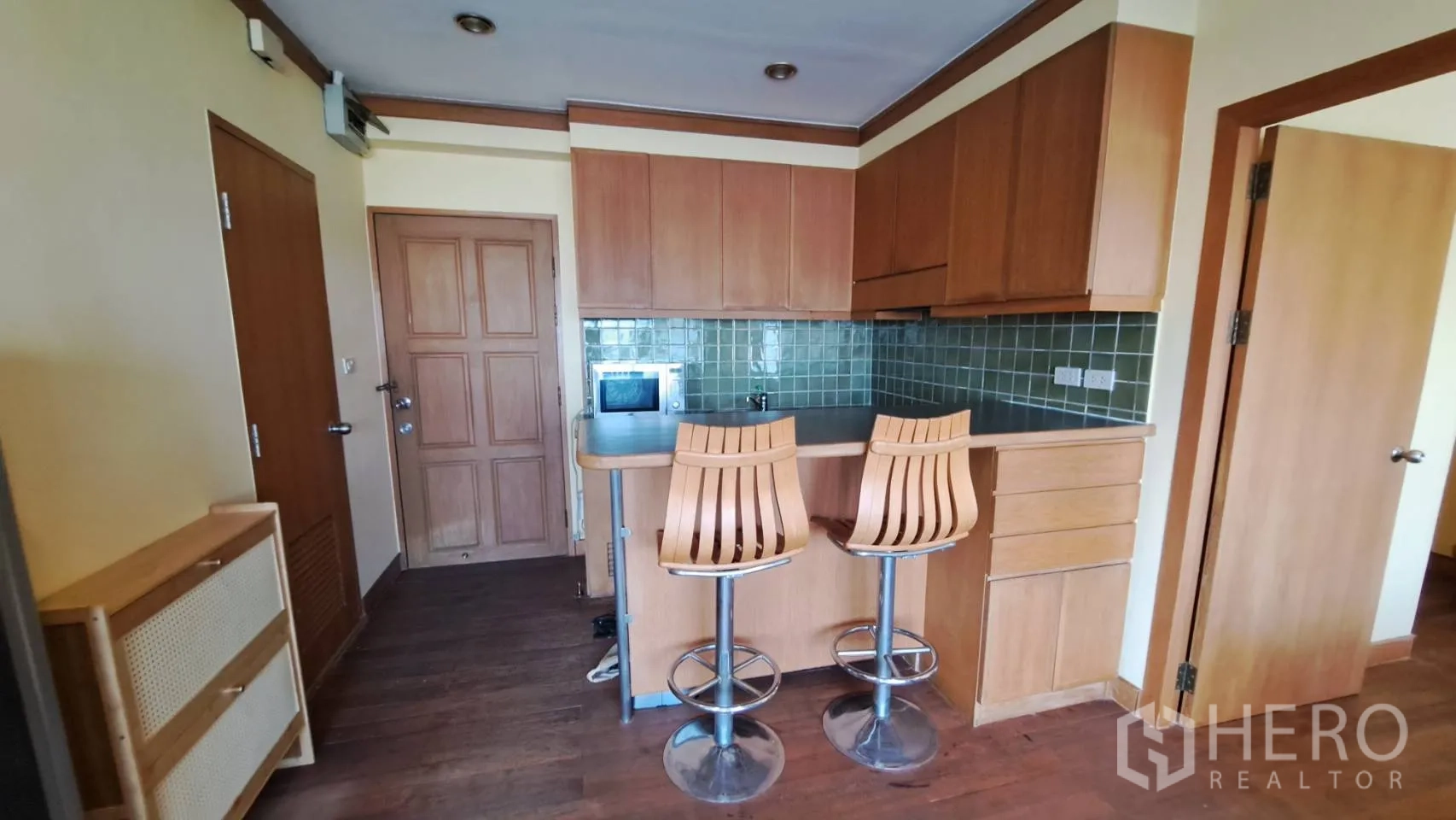 Condominium for rent in Khlong Toei, Bangkok - Kitchen area with bar seating, microwave, and ample storage cabinets.